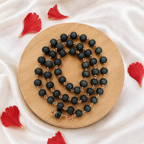 Black bead Mangalsutra necklace with copper-toned detailing arranged on a wooden display with red flowers