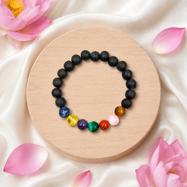 Handcrafted Karungali and 7 Chakra crystal bracelet displayed on a wooden base with sacred pink lotus flowers.
