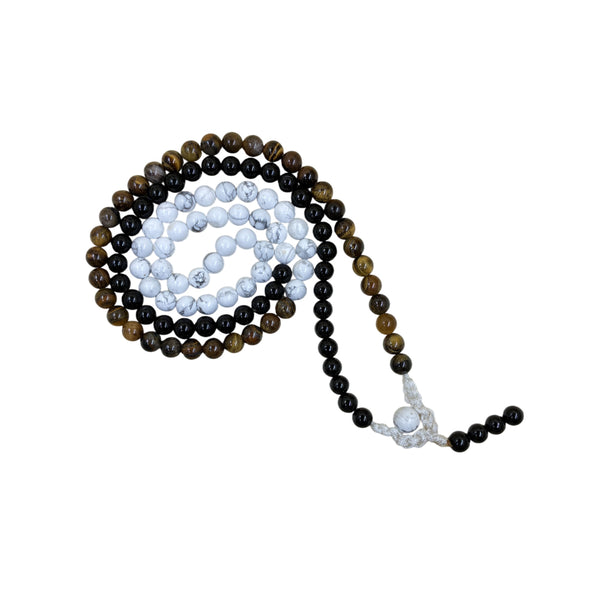A prayer mala coiled in a spiral, showcasing a blend of golden-brown Tiger's Eye, polished black, and white marbled Howlite crystal beads on a white background.