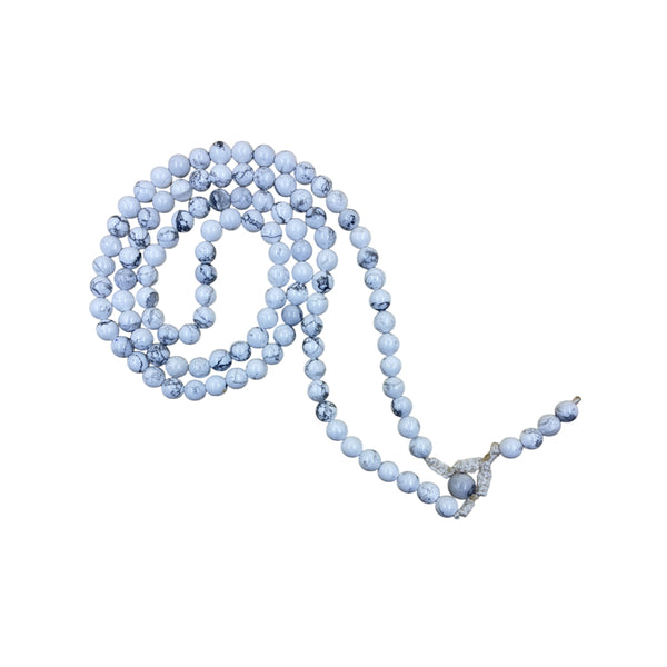 A traditional Howlite crystal prayer mala coiled in a spiral on a white background, showcasing the white stone beads with characteristic grey web-like patterns.