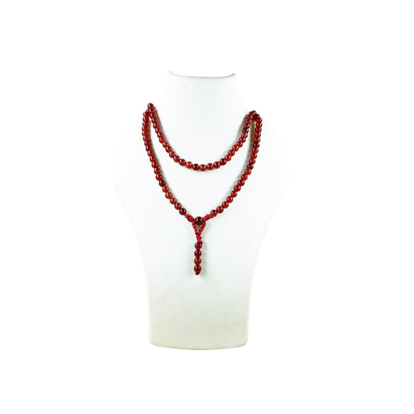 A Red Carnelian crystal prayer mala necklace worn doubled on a white jewelry display bust, highlighting the warm color and translucency of the stone.