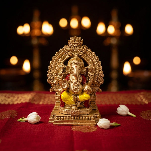 A 4-inch golden Ganesha statue with an intricate Prabhavali arch placed on a red traditional cloth with jasmine flowers and lit diyas in the background.