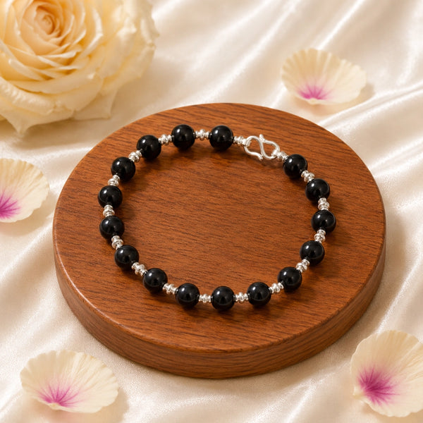 Angled view of a handcrafted Karungali ebony wood bracelet with polished silver-toned spacers on a wooden display