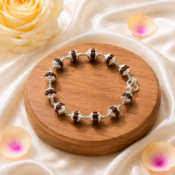 Handcrafted silver-toned Rudraksha healing bracelet displayed on a premium wooden base with decorative petals.