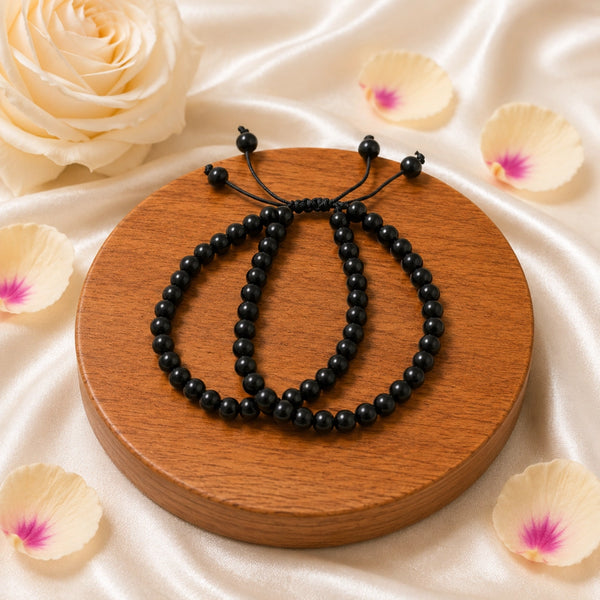 Black beaded bracelets on a wooden stand with white roses and petals in the background