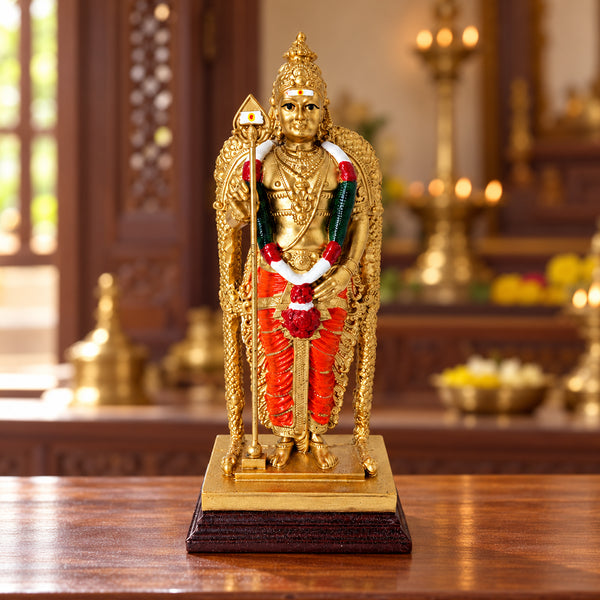Lord Murugan statue on a wooden table in a pooja room with brass lamps and flowers