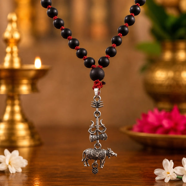 Close-up detail of the white metal Trishul, Damru, and Nandhi pendant on an authentic black karungali wood mala.