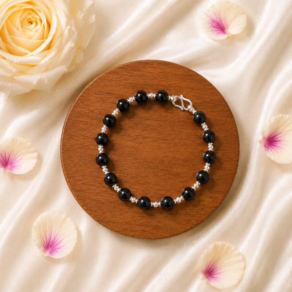 Overhead view of the Karungali silver-accented bracelet displayed with rose petals, highlighting the elegant 8mm beads