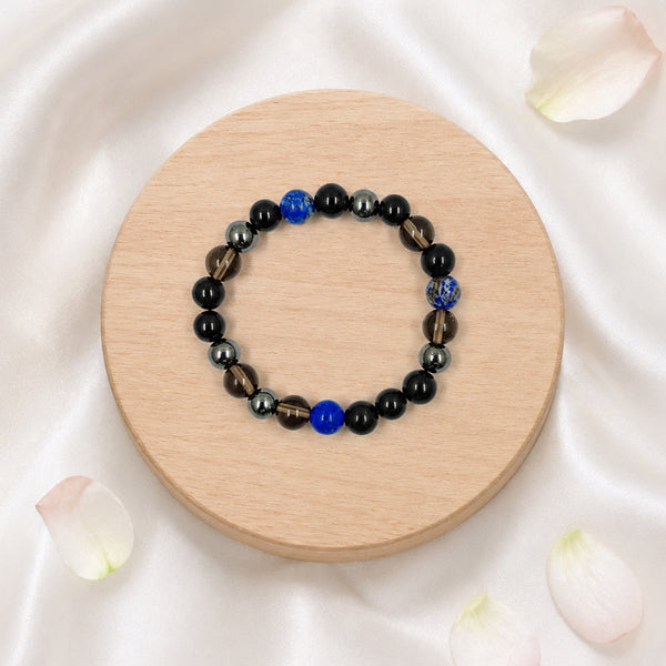Overhead view of the Shani Shakti crystal bracelet featuring lapis lazuli and black agate beads on a round wooden display.