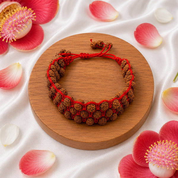 Handcrafted triple-row Rudraksha healing bracelet displayed with sacred Nagalinga flowers on white silk.