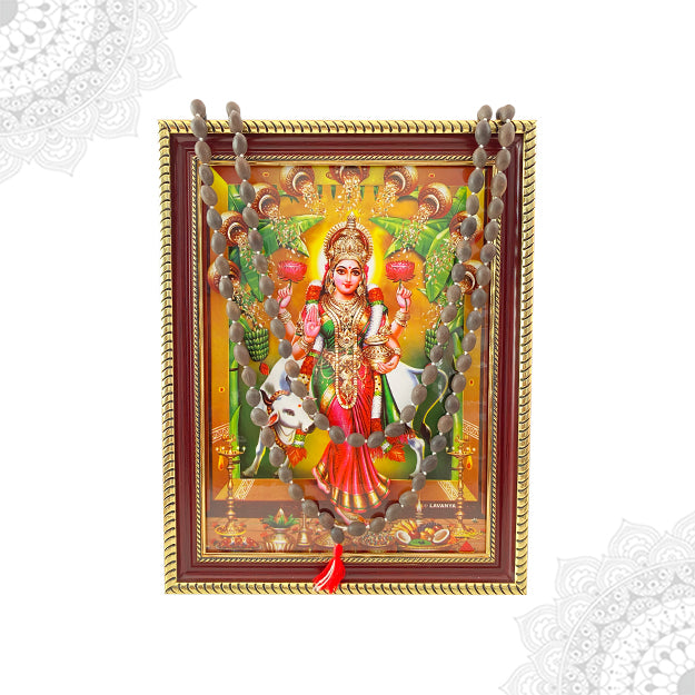 A colorful framed artwork depicting the goddess Vastu Grihalakshmi with a lotus bead malai hanging below.