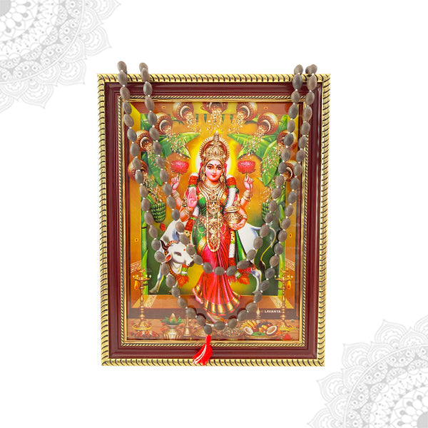 A colorful framed artwork depicting the goddess Vastu Grihalakshmi with a lotus bead malai hanging below.
